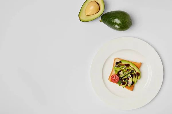 Top view of toast with avocados and cherry tomato on white plate on grey background — Stock Photo