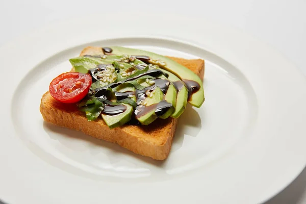 Fuoco selettivo di pane tostato con avocado e pomodoro ciliegia su piatto bianco — Foto stock