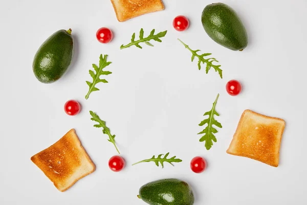 Vue de dessus des avocats, des feuilles d'arugulas, des toasts et des tomates cerises sur fond gris — Photo de stock