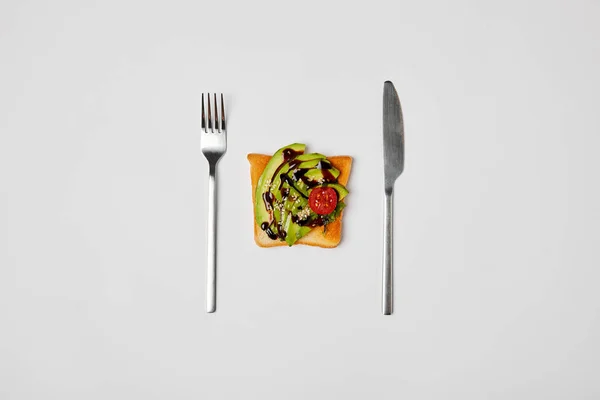 Top view of toast with avocado and cherry tomato, fork and knive isolated on grey — Stock Photo