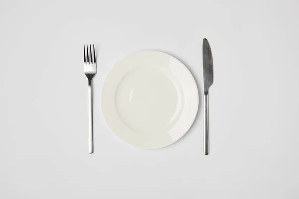 Top view of porcelain plate with fork and knive on grey background — Stock Photo