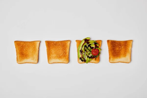 Draufsicht auf gegrillte knusprige Toasts mit Avocado und Kirschtomaten auf grauem Hintergrund — Stockfoto