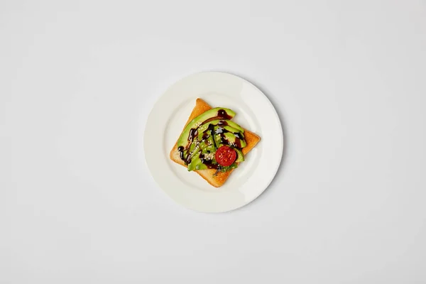 Draufsicht auf Toast in Teller mit Avocado und Kirschtomaten auf grauem Hintergrund — Stockfoto