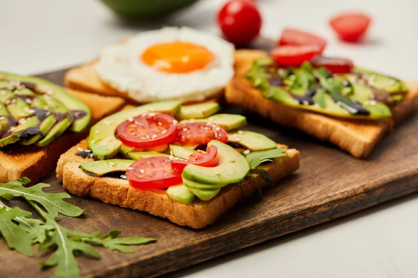 Selective focus of cutting board with toasts, scrambled egg, cherry tomatoes and avocado on white background — Stock Photo