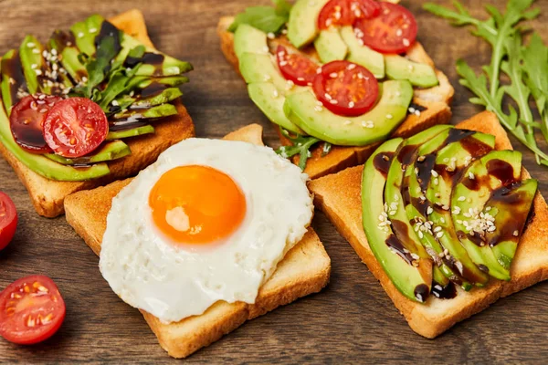Вибірковий фокус тостів з яєчним кремом, вишневими помідорами та авокадо на дерев'яному фоні — стокове фото