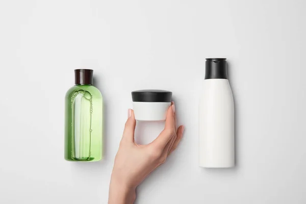 Top view of female hand near cream container with different cosmetic bottles on white background — Stock Photo