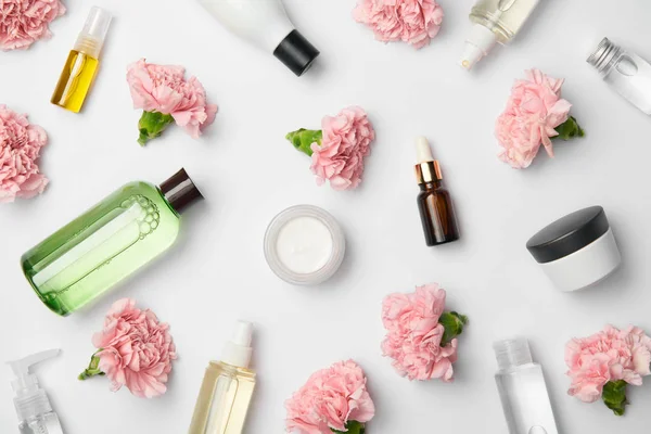 Vue du dessus de divers récipients cosmétiques et fleurs d'oeillets roses sur fond blanc — Photo de stock