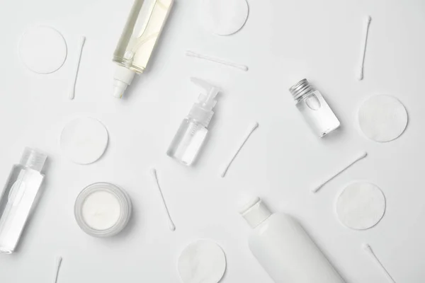 Vista superior de diferentes recipientes cosméticos, palitos de algodão e almofadas cosméticas no fundo branco — Fotografia de Stock