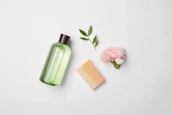 Vista superior de diferentes botellas de cosméticos, jabón, rama de planta de té y flor de clavel sobre fondo blanco - foto de stock
