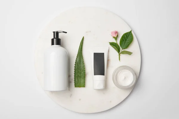 Vue de dessus de différents récipients cosmétiques, feuille d'aloe vera et fleur de rose sur surface ronde blanche — Photo de stock