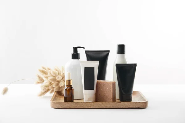 Holztablett mit verschiedenen Kosmetikbehältern und Stacheln auf weißer Oberfläche — Stockfoto