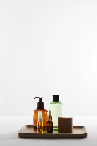 Vassoio in legno con vari contenitori cosmetici e sapone su superficie bianca — Foto stock