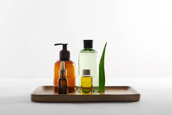 Holztablett mit verschiedenen Kosmetikbehältern und Aloe Vera Blatt auf weißem Hintergrund — Stockfoto