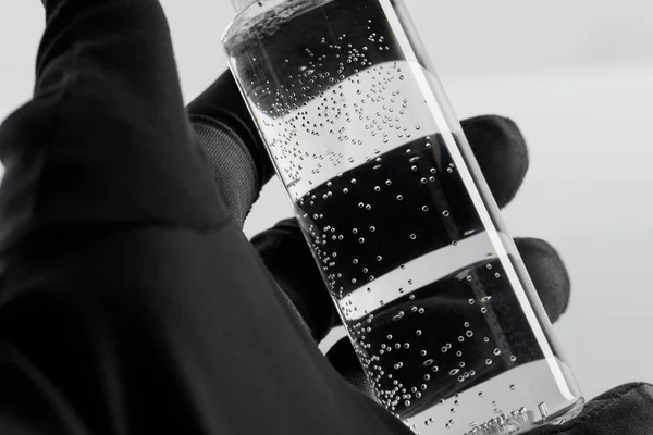Abgeschnittene Ansicht der weiblichen Hand in schwarzem Handschuh mit transparenter Kosmetikflasche auf weißem Hintergrund — Stockfoto