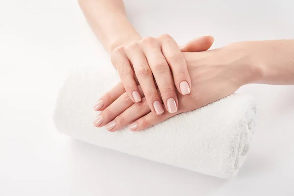 Vista parcial de las manos femeninas sobre rizo suave toalla enrollada sobre fondo blanco - foto de stock