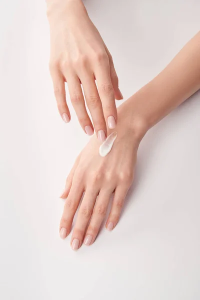 Vista parcial de la mujer aplicando crema cosmética sobre fondo blanco — Stock Photo