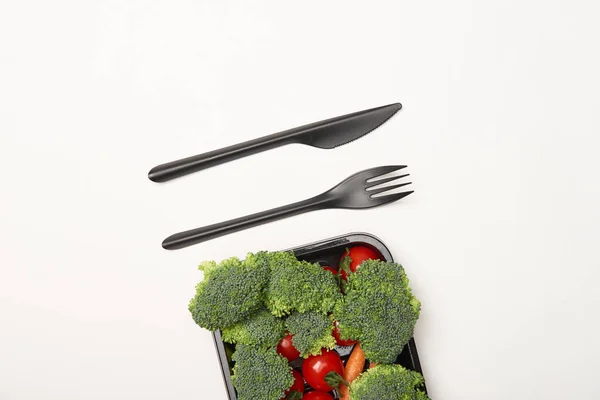 Top view of black cutlery and vegetables in bowl isolated on white — Stock Photo