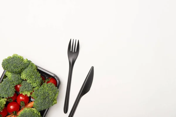 Верхний вид овощей в черной миске и столовые приборы на белом фоне — стоковое фото