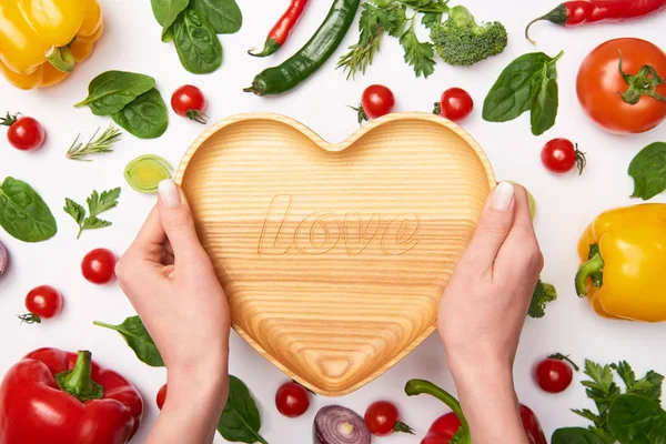 Partial view of woman holding wooden cutting board and vegetables on white background — Stock Photo