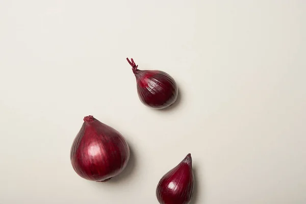 Vue du dessus de trois oignons rouges sur fond gris — Photo de stock