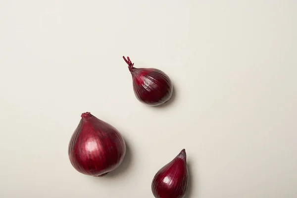Top view of three red onions on grey background — Stock Photo