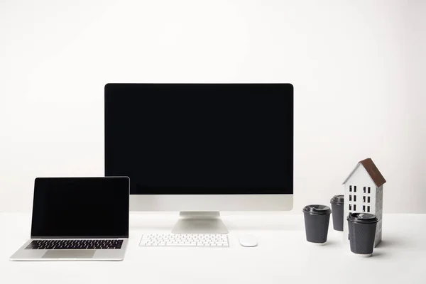 Local de trabalho com café para ir, modelo de casa, computador desktop e laptop com espaço de cópia isolado em branco — Fotografia de Stock