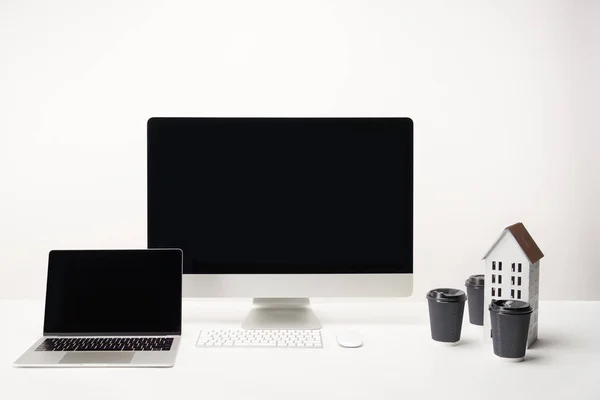 Workplace with coffee to go, house model, desktop computer and laptop with copy space isolated on white — Stock Photo