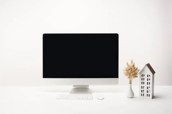 Posto di lavoro con modello di casa, fiori secchi in vaso e computer desktop con spazio copia isolato su bianco — Foto stock