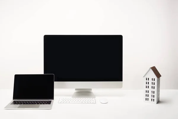 Lugar de trabajo con modelo de casa, computadora de escritorio y portátil con espacio de copia aislado en blanco - foto de stock