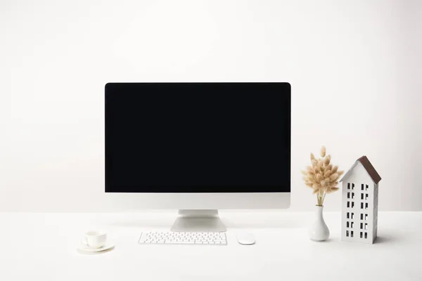 Lugar de trabajo con modelo de casa, flores secas, taza de café y computadora de escritorio con espacio de copia aislado en blanco - foto de stock