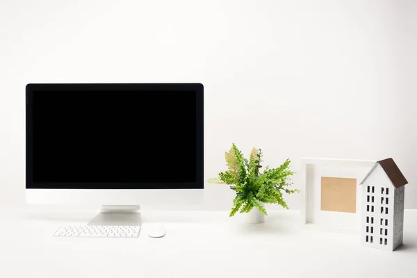 Lieu de travail avec usine, modèle de maison, cadre photo et ordinateur de bureau avec espace de copie isolé sur blanc — Photo de stock