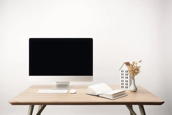 Lugar de trabajo con flores secas, modelo de casa, portátil y computadora de escritorio con espacio de copia aislado en blanco - foto de stock