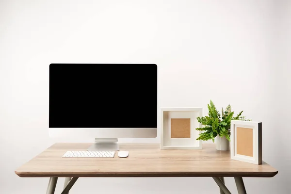 Lugar de trabajo con marcos de fotos, planta verde y computadora de escritorio con espacio de copia aislado en blanco - foto de stock