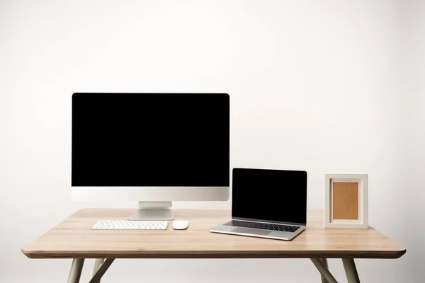 Робоче місце з фоторамкою, настільним комп'ютером і ноутбуком з копіювальним простором на дерев'яному столі ізольовано на білому — стокове фото