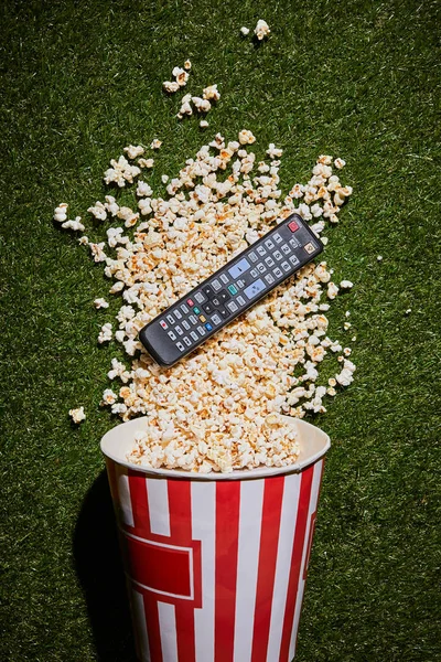 Top view of tasty popcorn lying near remote control on green grass — Stock Photo