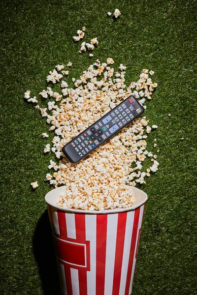 Blick von oben auf leckeres Popcorn, das in der Nähe der Fernbedienung auf grünem Gras liegt — Stockfoto