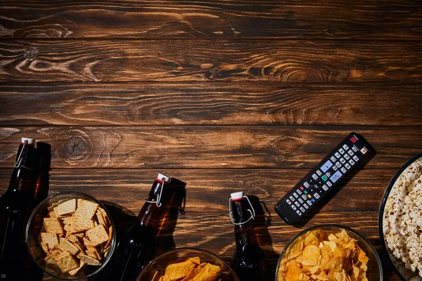 Vista superior de lanches saborosos perto de garrafas e controle remore na mesa de madeira — Fotografia de Stock