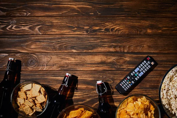 Vista superior de sabrosos aperitivos cerca de botellas y control remore en mesa de madera - foto de stock