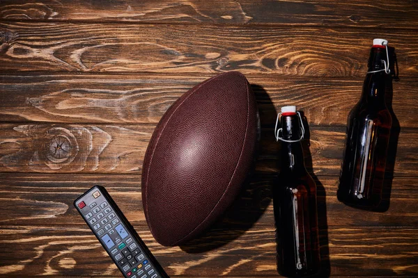 Vista superior da garrafa marrom com cerveja perto da bola e controle remoto na mesa de madeira — Fotografia de Stock