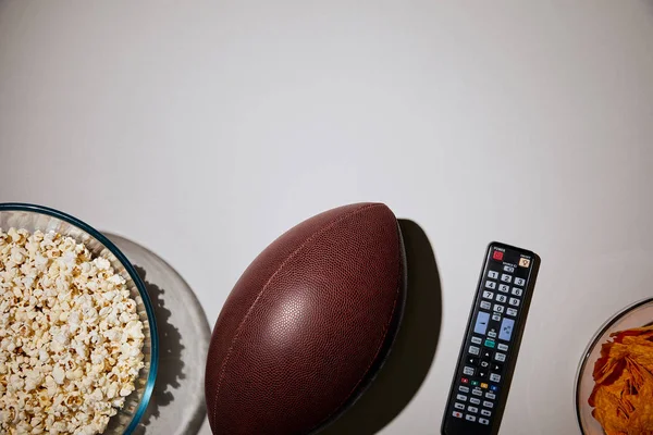 Верхний вид попкорна в миске рядом мяч и пульт дистанционного управления на белом фоне — стоковое фото