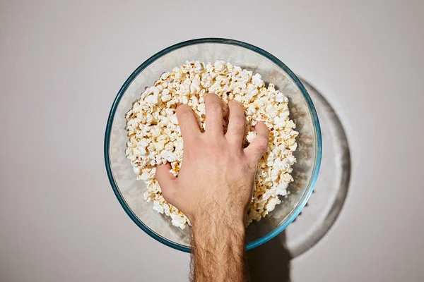 Cropped view of man putting hand in glass bowl with popcorn on white background — Stock Photo