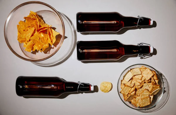 Vista superior de garrafas com cerveja perto de lanches saborosos no fundo branco — Fotografia de Stock