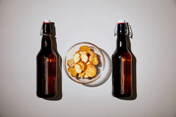 Top view of brown bottles with beer near snack in bowl on white background — Stock Photo