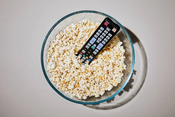 Top view of tasty popcorn in bowl with remote control on white background — Stock Photo