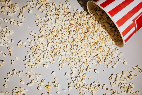 Vista dall'alto di gustosi popcorn sdraiati vicino alla tazza di popcorn su sfondo bianco — Foto stock