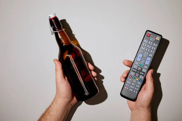 Cropped view of man holding bottle with beer and remote control in hands on white background — Stock Photo