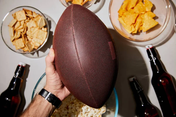 Foco seletivo do homem segurando bola marrom perto de lanches e bebidas no fundo branco — Fotografia de Stock