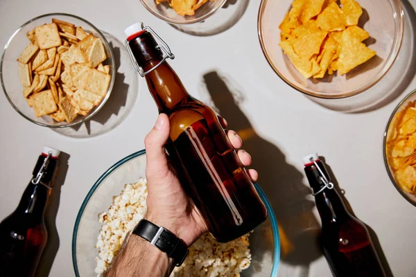 Selective focus of man holding bottle with beer near snacks in bowls on white background — Stock Photo