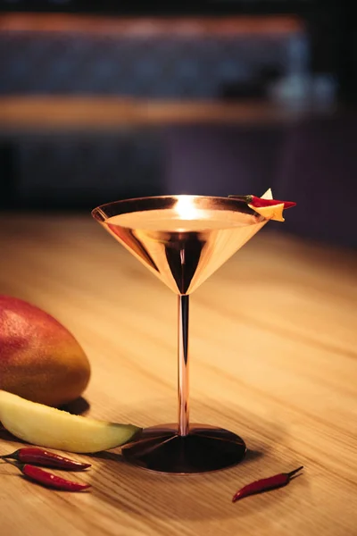 Selective focus of alcoholic cocktail in metal glass decorated with chili pepper, nacho chip and mango on wooden table — Stock Photo