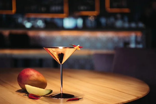 Selective focus of alcoholic cocktail in metal glass decorated with chili pepper, nacho chip and mango on wooden table — Stock Photo